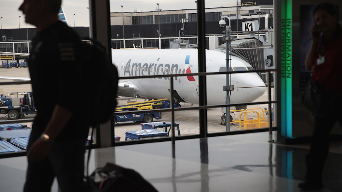 flyers walk through an airport with an american airlines passenger plane in the background