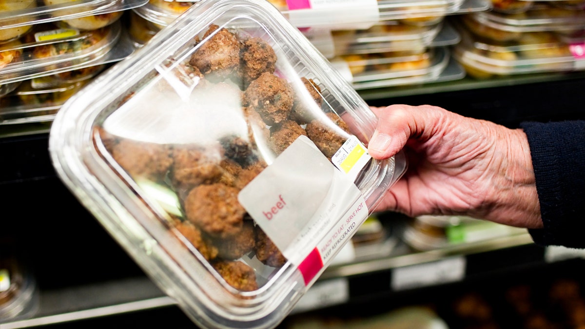 An aged  woman's manus  holds a bundle  of ready-to-eat beef astatine  a market  store.