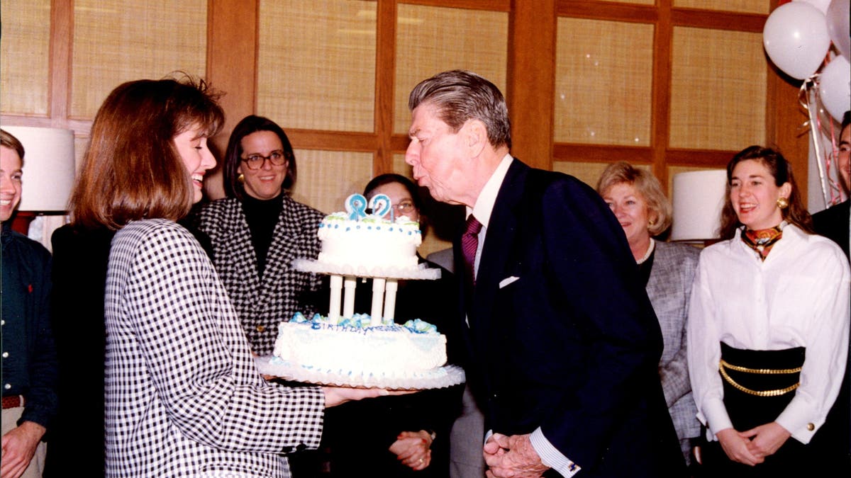 Peggy Grande holds a cake for President Ronald Reagan's 82nd birthday in his Century City, California, office after his second term was completed.