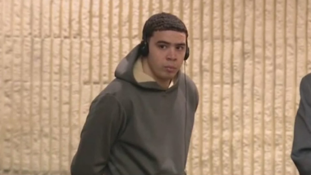 Murder suspect Eric German-Pena wearing headphones and a gray hoodie, with his arms handcuffed behind his back