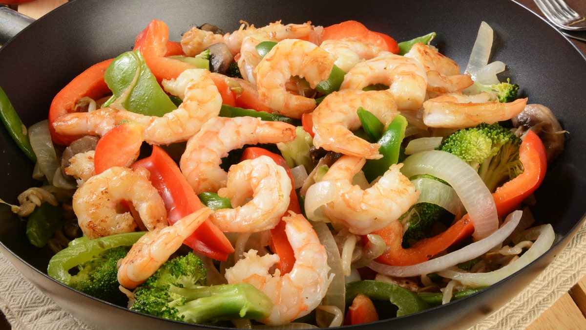 Esta es una imagen de salteado de camarones y verduras en un wok.