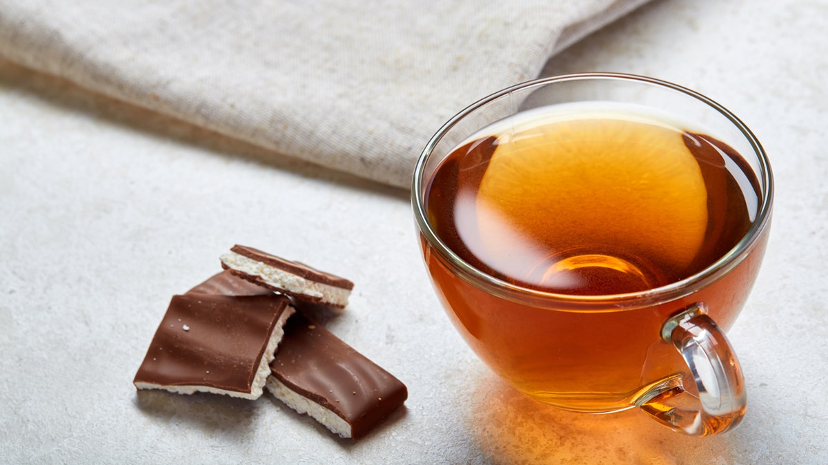 Pieces of chocolate sit next to a glass of tea and a napkin on a table.