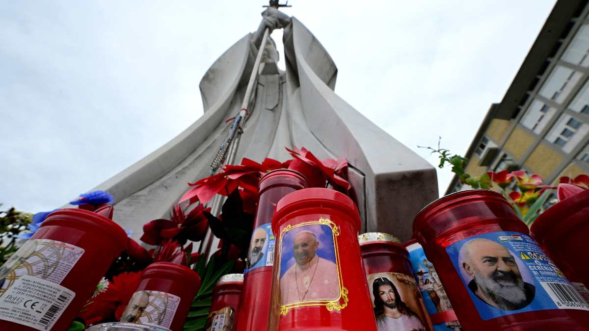 Una vela con un retrato del Papa Francisco se establece en la parte inferior de una estatua del Papa Juan Pablo II en el Hospital Gemelli, donde el Papa Francisco es hospitalizado por pruebas y tratamiento para la bronquitis, en Roma el 17 de febrero de 2025. 