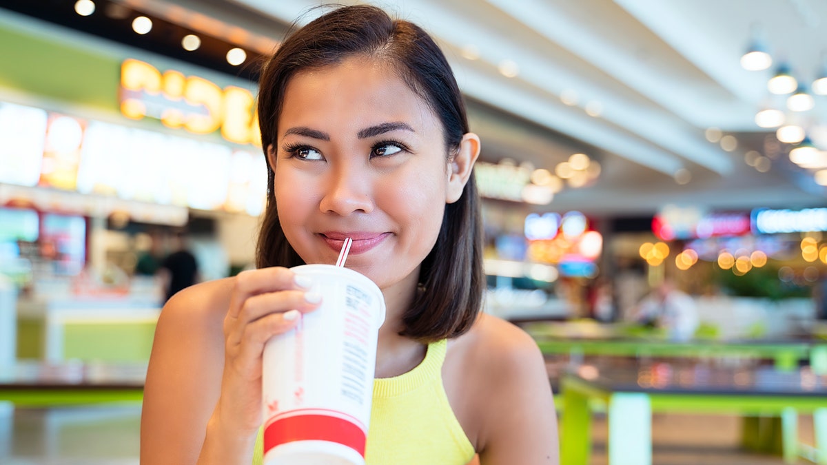 A woman smiles as she drinks a soda from a straw at a fast-food restaurant.