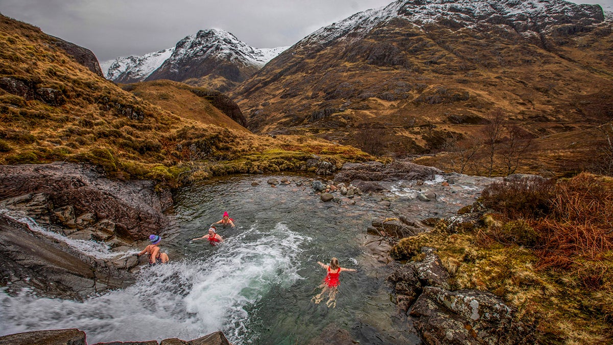 People swim in rivers surrounded by nature, hills, mountains