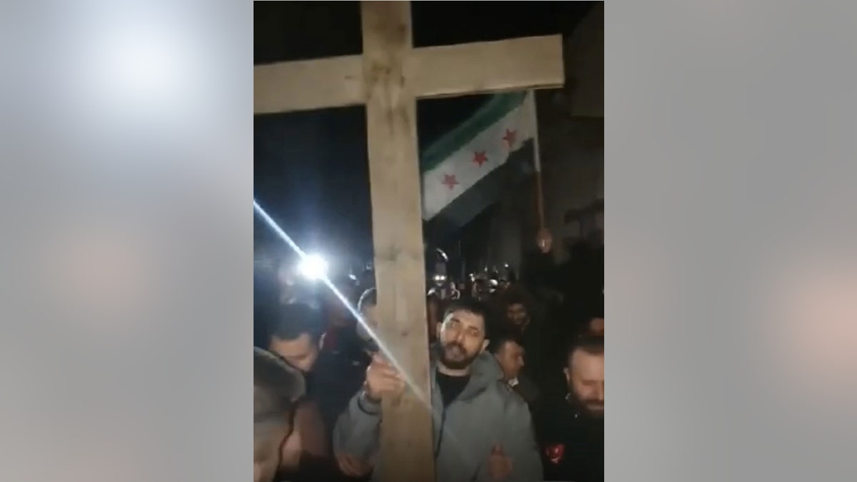 A wooden cross and Syrian flag are seen at an Eagles of Antioch protest in Damascus in December 2024.