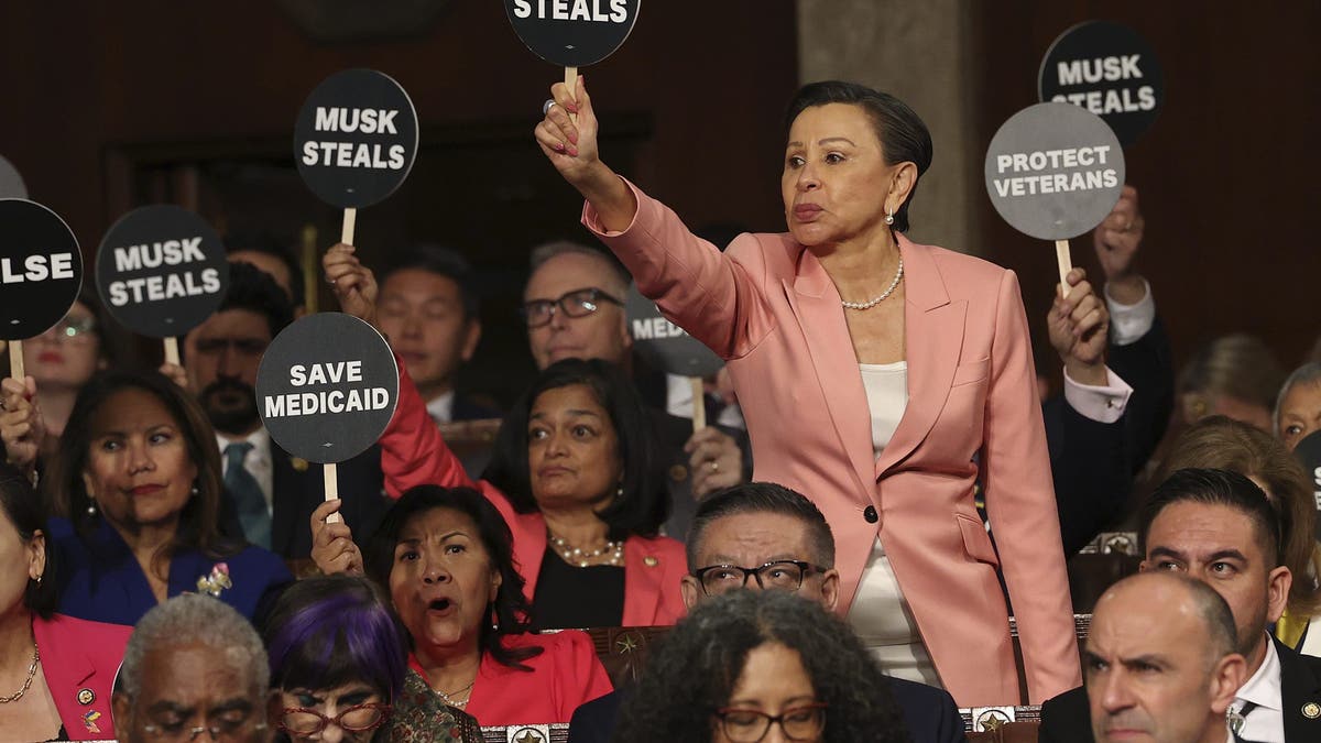 Rep. Nydia Velazquez, D-N.Y., holds a protest sign with fellow Democrats as President Donald Trump addresses a joint session of Congress at the Capitol in Washington, Tuesday, March 4, 2025. (Win McNamee/Pool Photo via AP)