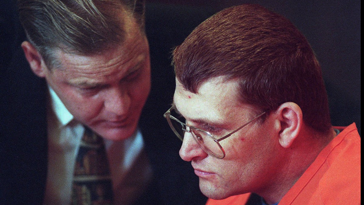 A picture close to Keith Jassonon in an orange suit listens to his lawyer.