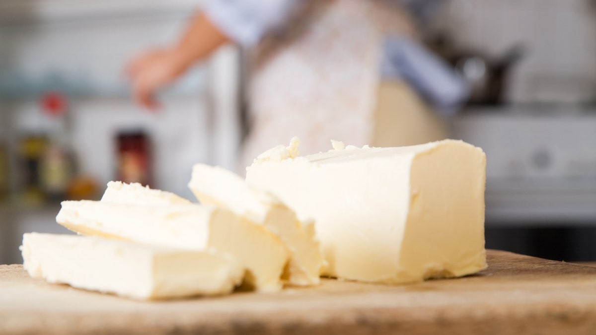 A close-up view of butter slices as a woman is seen in the background opening the refrigerator.