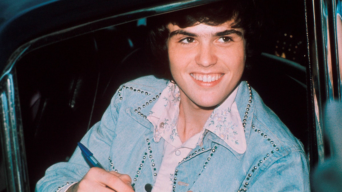 Close up of Donny Osmond signing autographs in a car