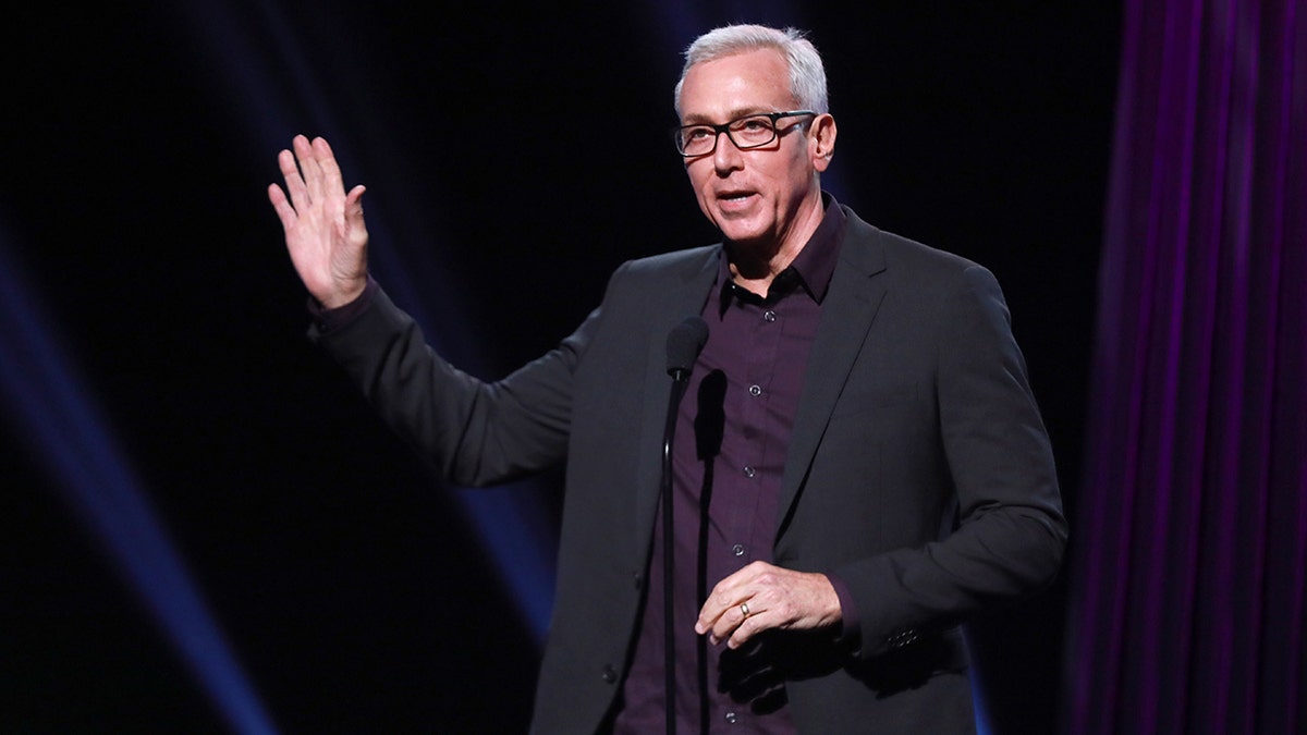 Dr. Drew giving a speech on stage wearing a black blazer.