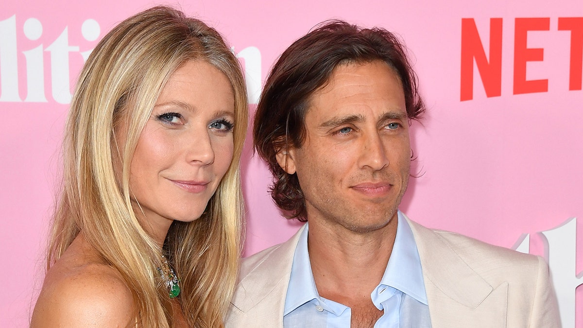 A close-up of Gwyneth Paltrow posing with her husband in front of a pink Netflix step and repeat.