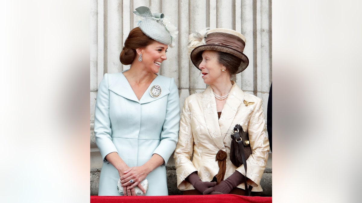 Kate Middleton wearing a pale blue dress smiling at Princess Anne wearing an ivory dress with a matching brown hat.