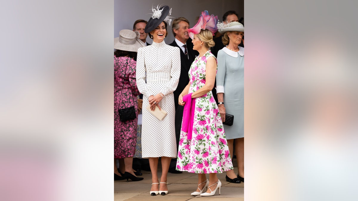 Kate Middleton in a polka dot dress and a matching hat standing and laughing with Sophia in a floral dress and a matching pink hat.