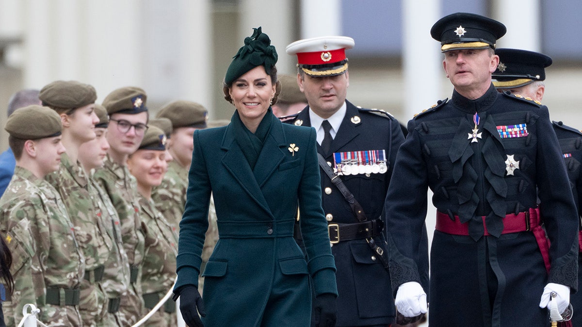 Kate Middleton walking next to men in uniform in a dark green coat during the St. Patrick's Day parade