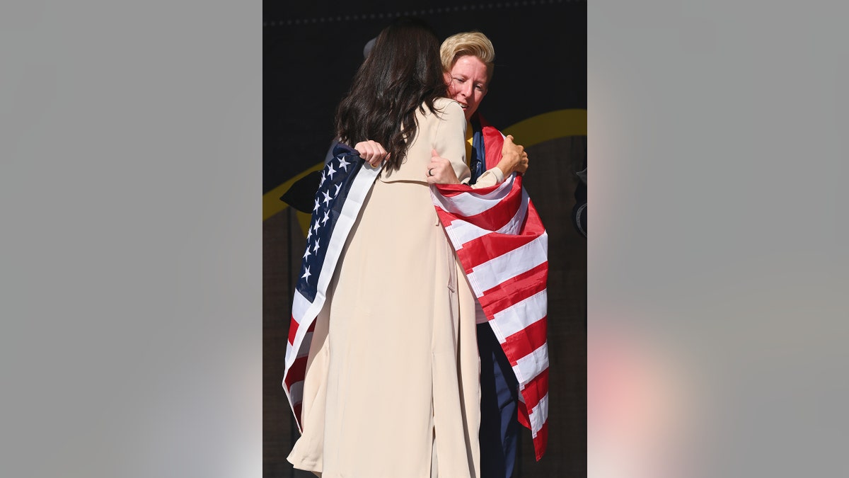 Meghan Markle hugging a woman with an American flag wrapped around them.