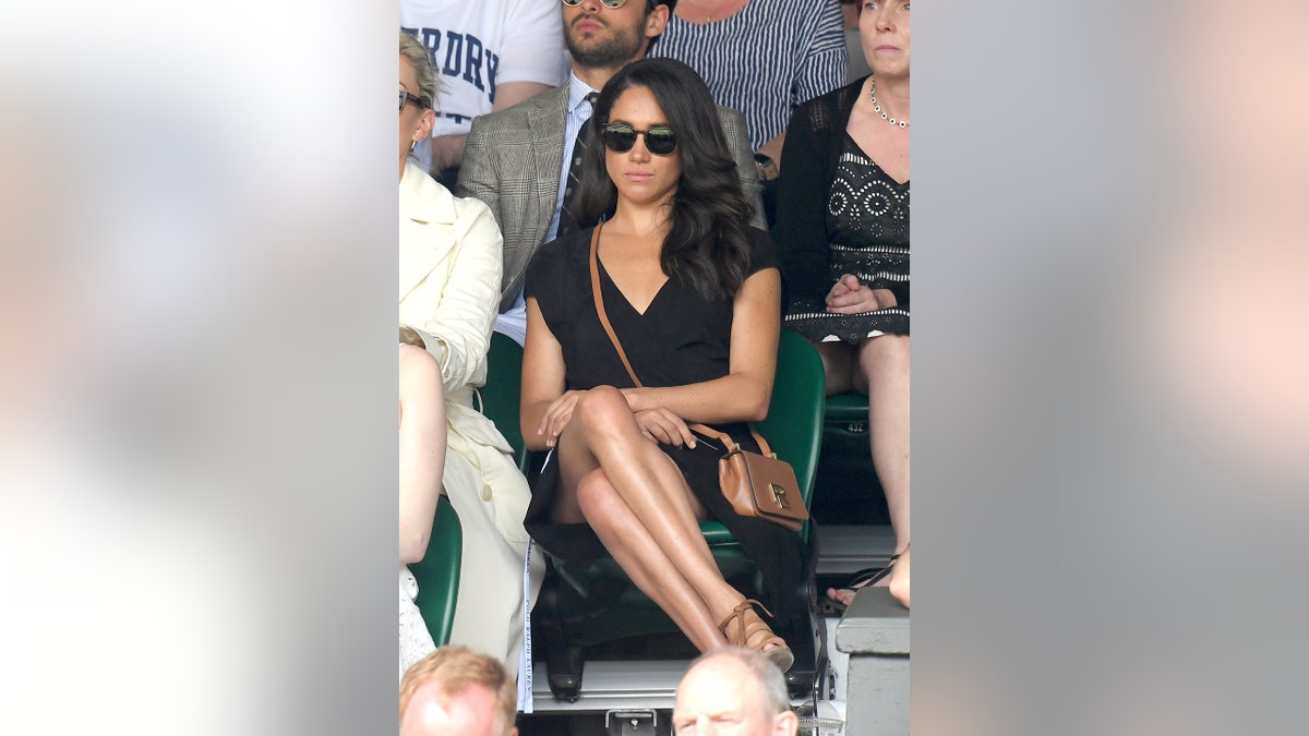 Meghan Markle sitting down wearing a black dress and sunglasses