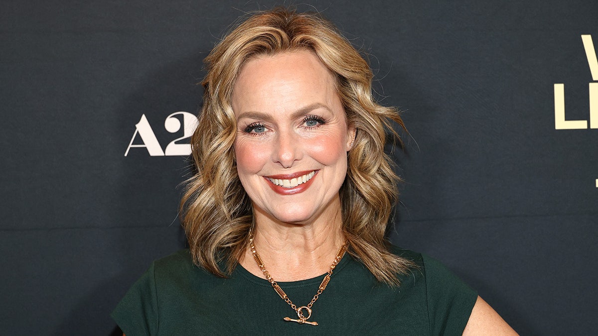 A close-up of Melora Hardin smiling in a hunter green dress and a gold chain.