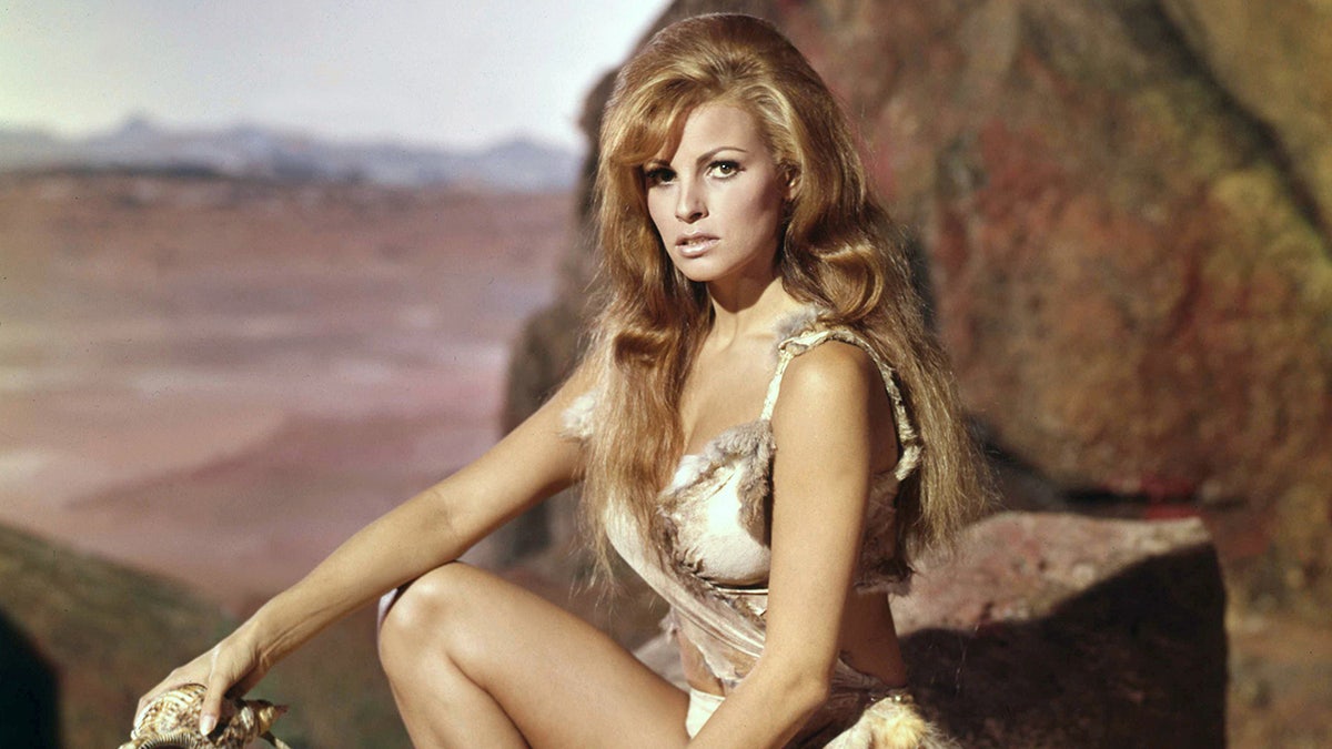 Raquel Welch in a fur bikini posing outdoors.