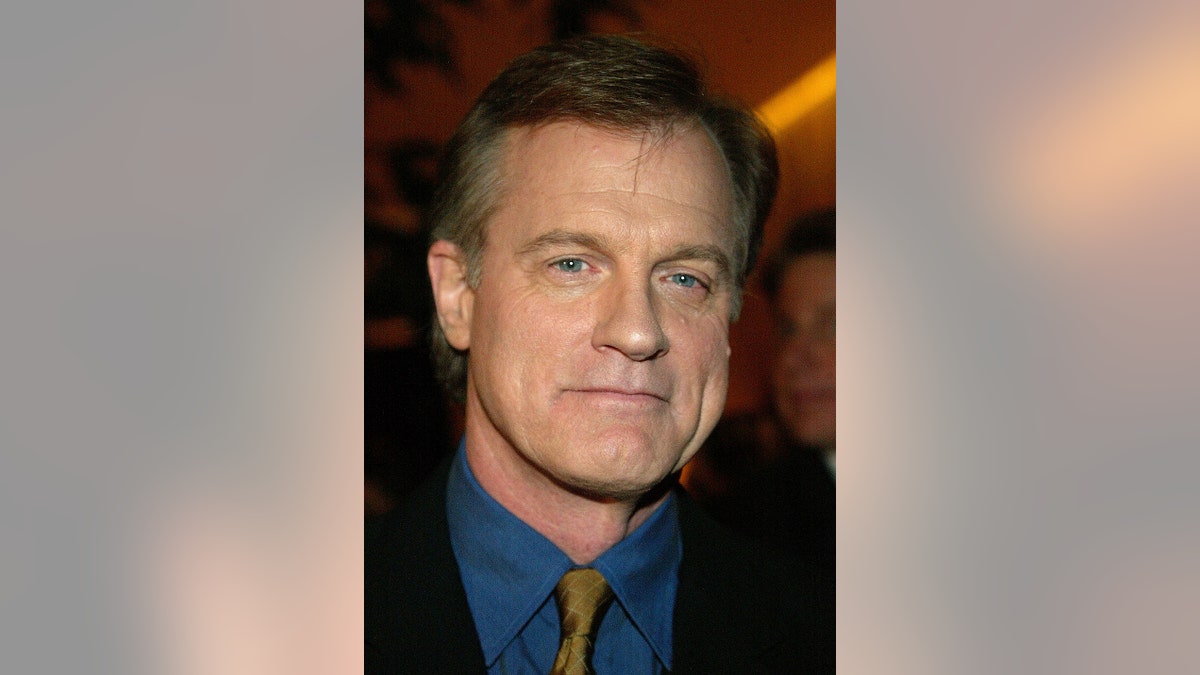 A close-up pf Stephen Collins wearing a black jacket and a blue shirt with a cold tie.