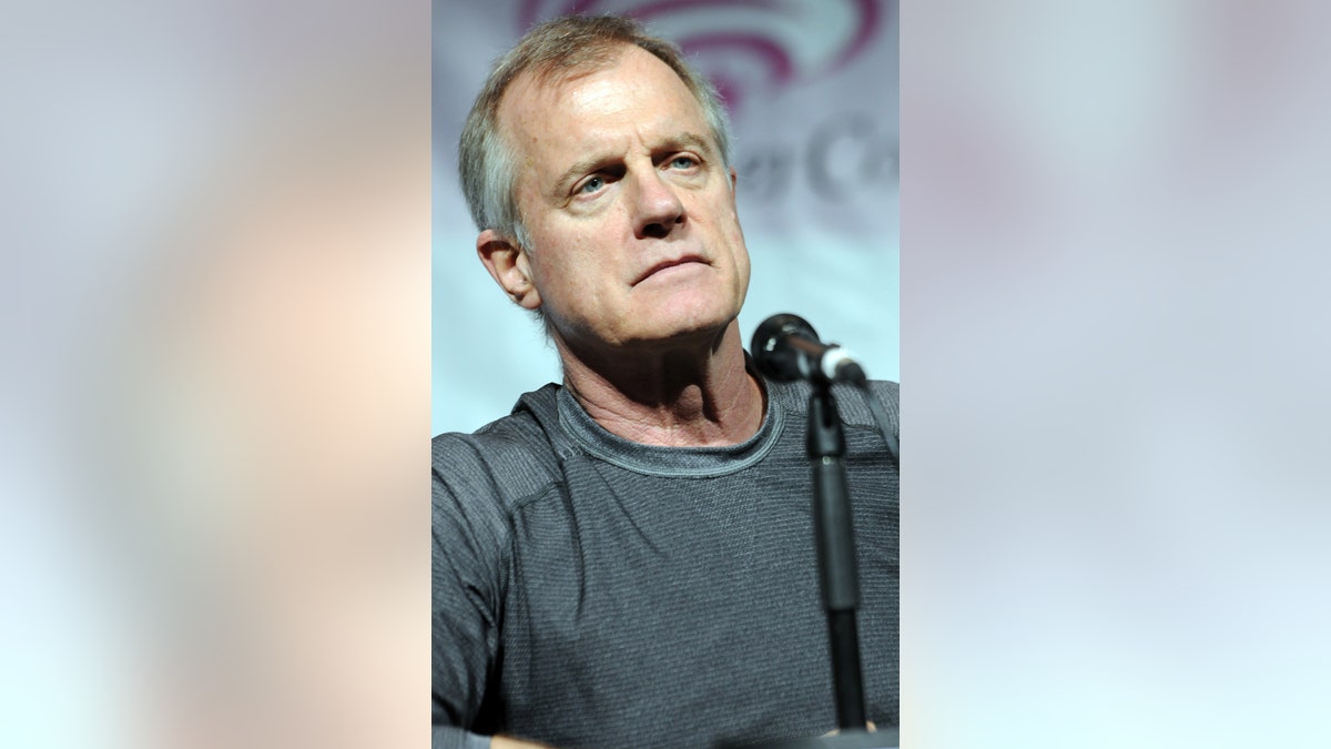 Stephen Collins wearing a grey sweater and speaking to a mic.