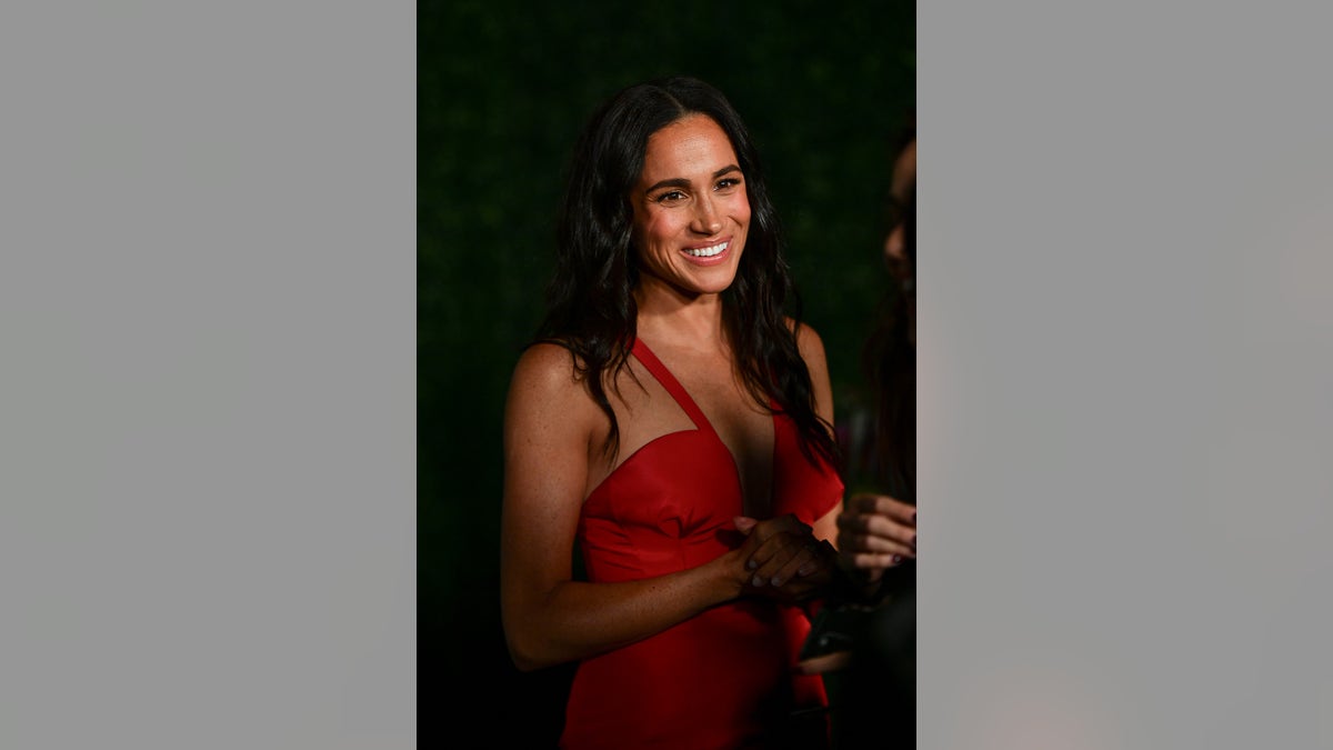 Meghan Markle smiling and wearing a red strappy dress.