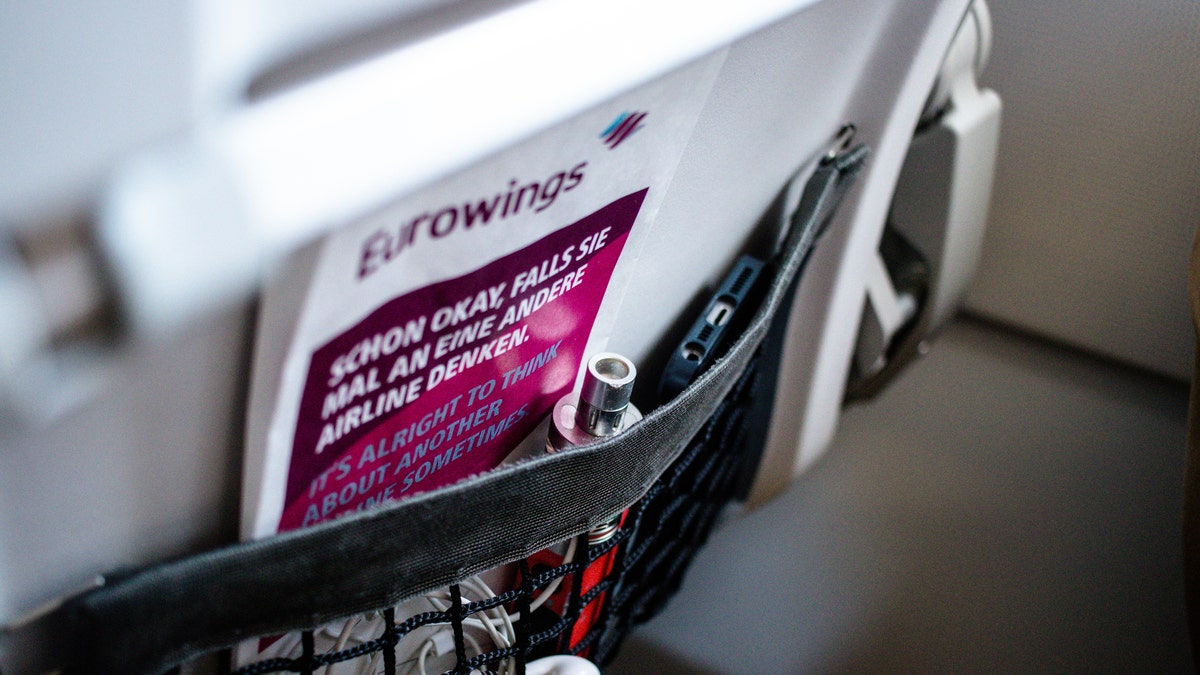 View of a Eurowings airplane seat's back paper holder. Promotional material, earphones, mobile phone and e-cigarette (vape). Smoking is prohibited on airplanes, even with e-cigarettes.