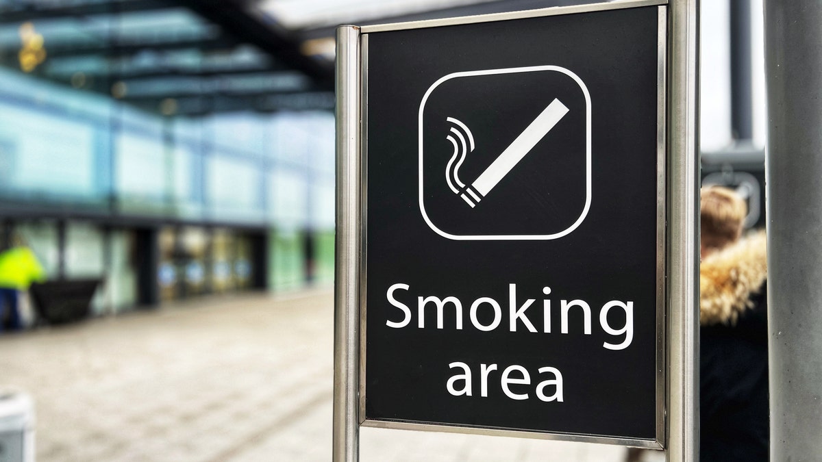 A sign indicating a smoking area is shown inside an airport.