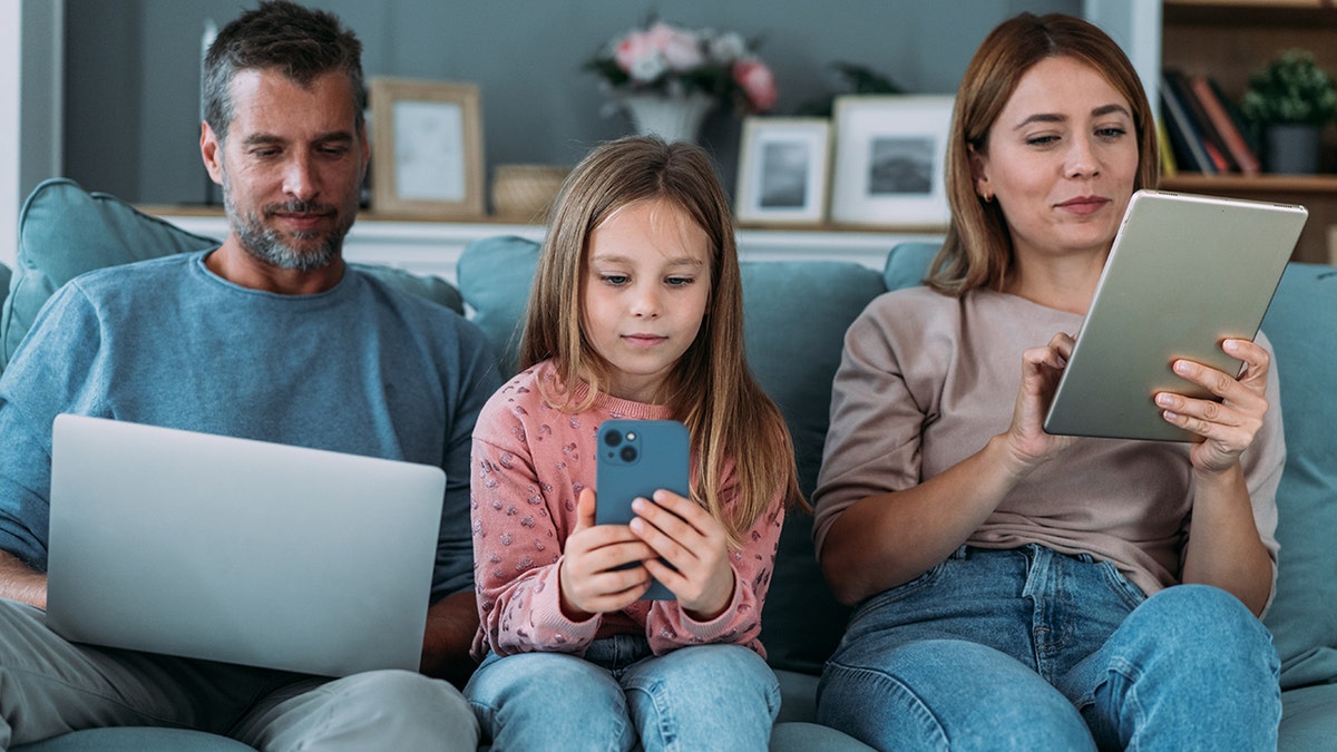 Family with a child sitting on the sofa in the living room and using different devices