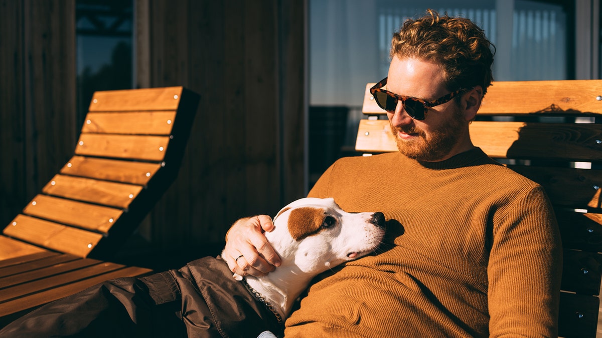 Man in sunglasses binding with a dog on a wooden bench.