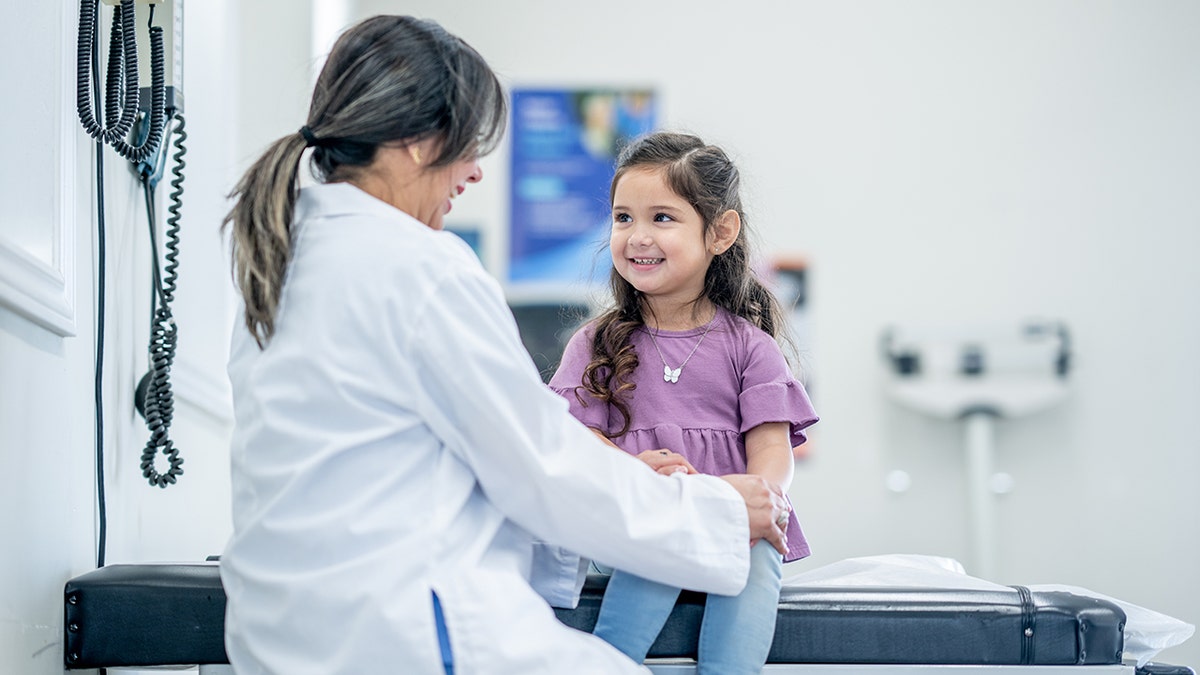 girl sits up on an exam table in front of her doctor