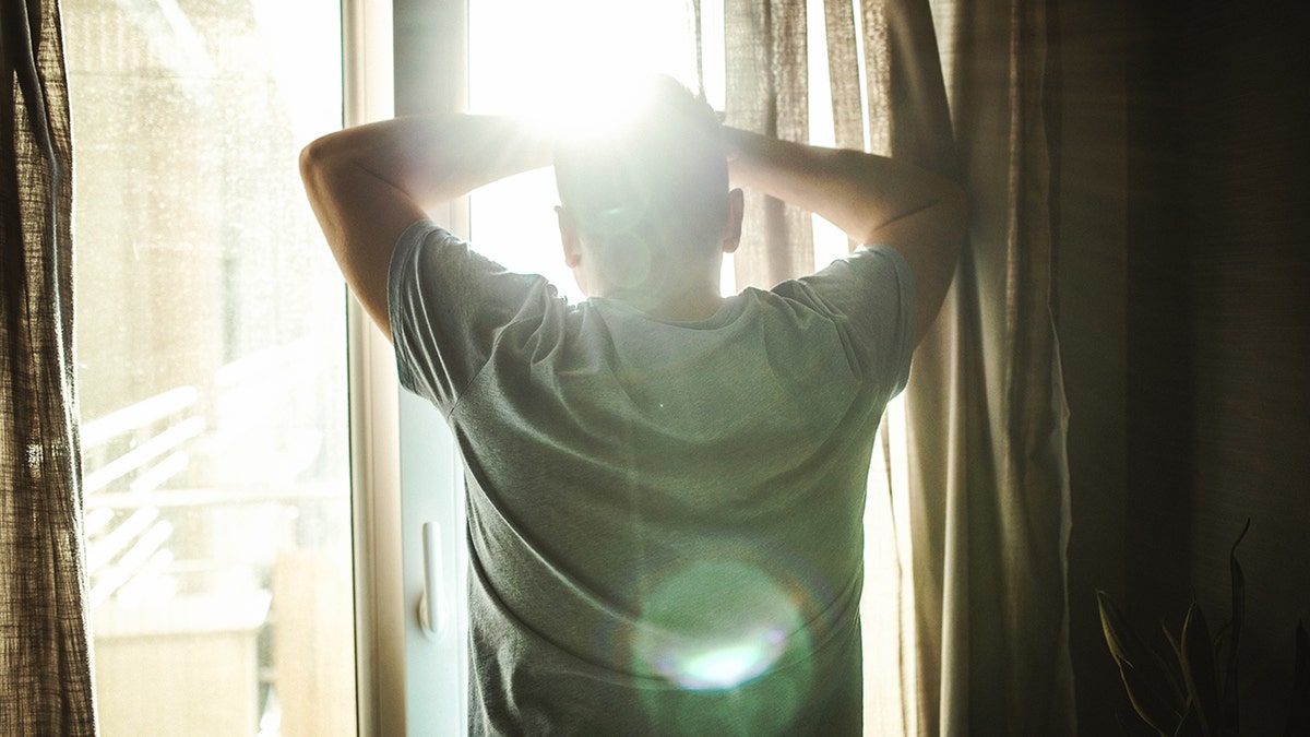 man looking through window in bedroom