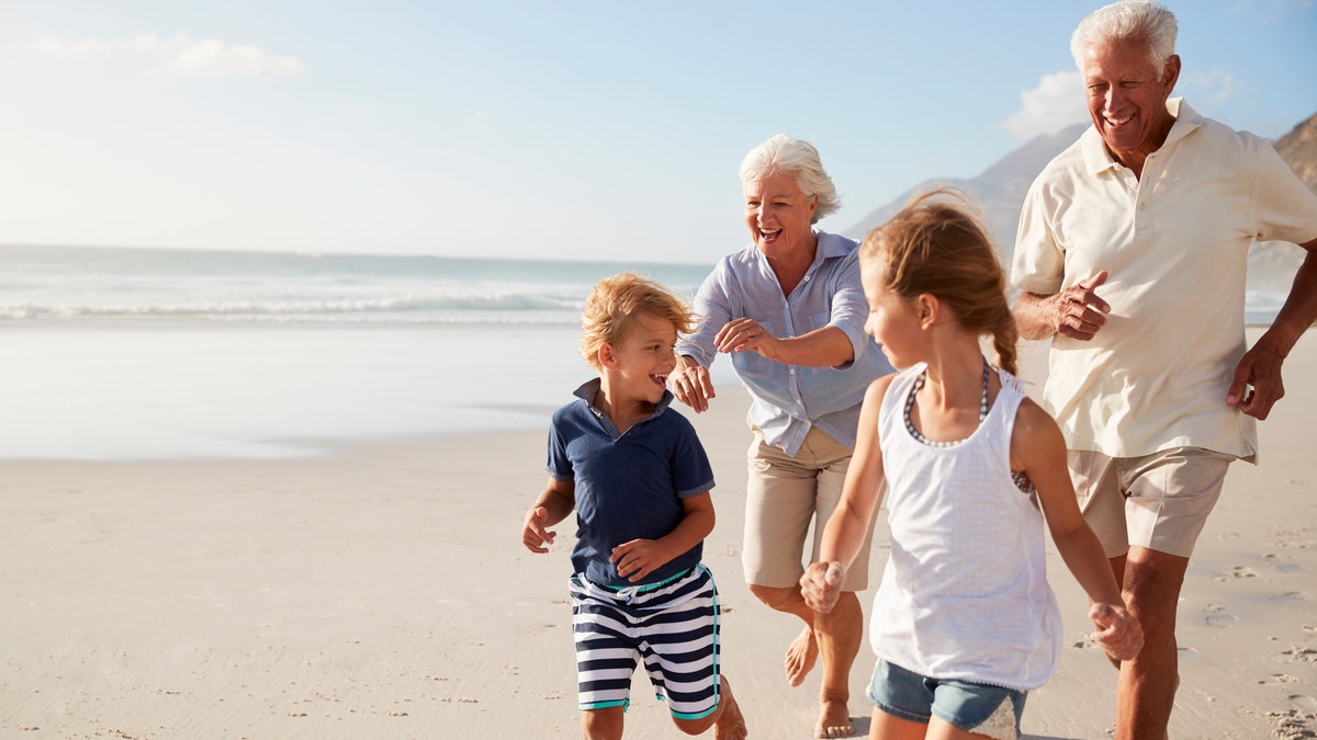 Grandparents Running Along Beach With Grandchildren On Summer Vacation