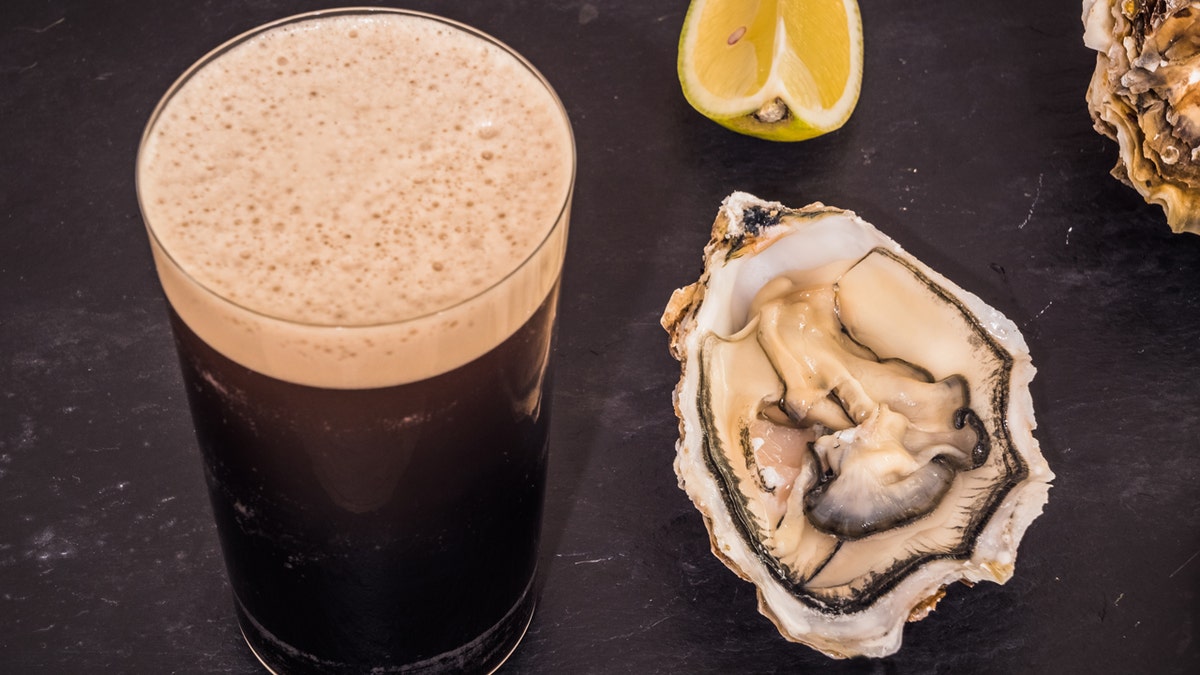 A glass of stout next to an oyster.