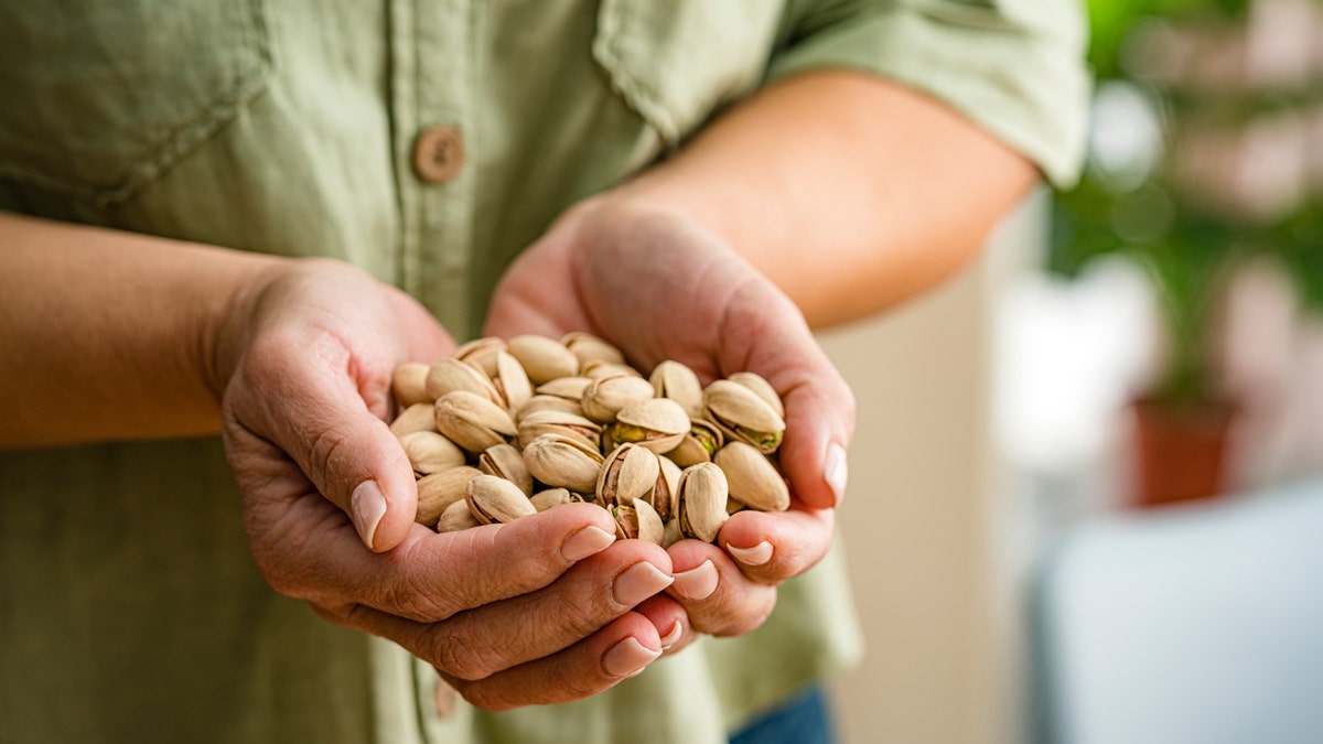 A hand holds pistachios.