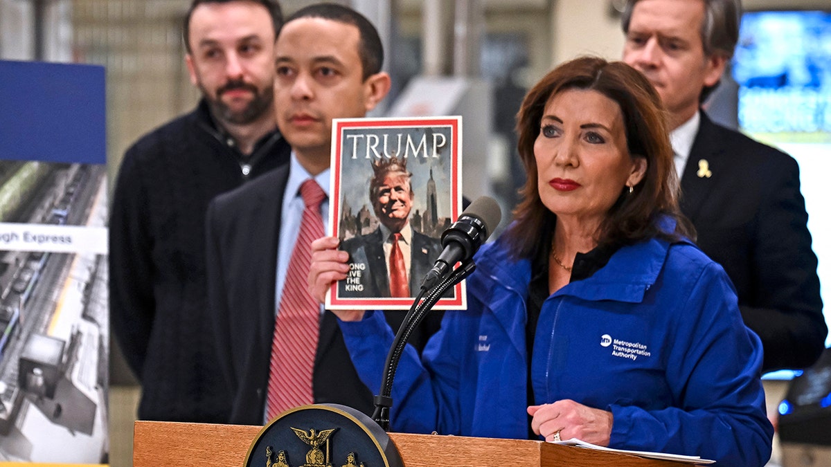 Kathy Hochul holding a photo of Trump with a crown