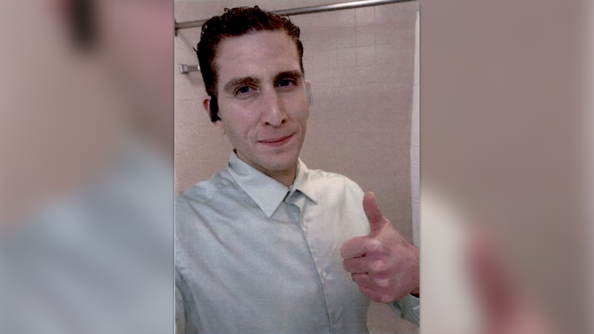 Bryan Kohberger gives a thumbs up in a selfi photo, wearing a buttoned up shirt and earbugs, in front of an empty shower.