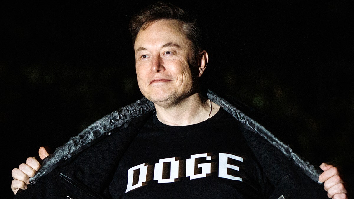 Elon Musk smiles while offering it "Dodge" shirt