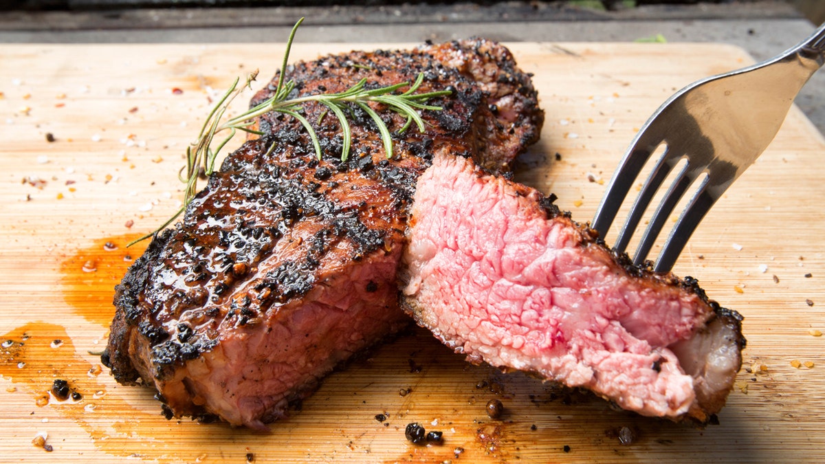 A New York strip steak is on a cutting board with a fork in it.