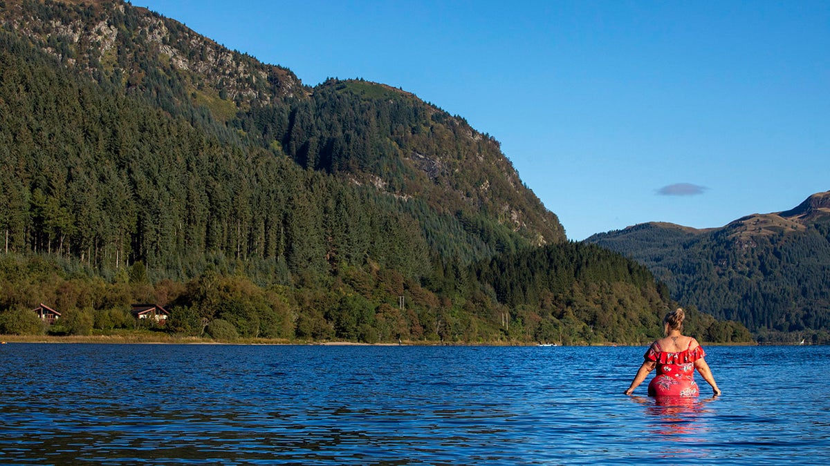 Woman standing in the lake, staring at the mountains