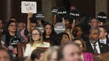 Democrats hold protest signs as President Donald Trump addresses a joint session of Congress at the Capitol in Washington, Tuesday, March 4, 2025. (Win McNamee/Pool Photo via AP)