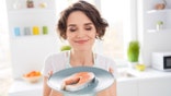 A woman with her eyes closed holds a fillet of salmon on a blue plate