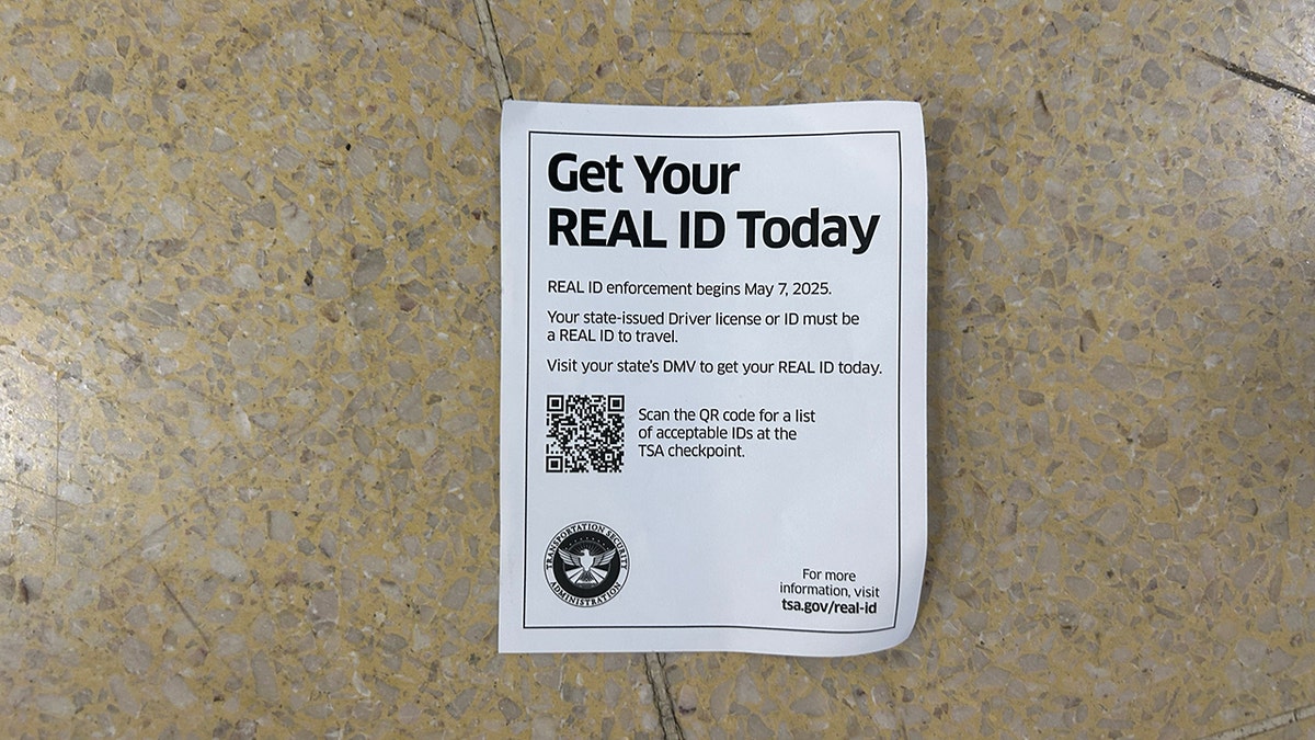 A paper leaflet on the ground encourages travelers to upgrade to a real identifier. Read: "Get your real knowledge today, the real knowledge enforcement begins on May 7, 2025. Your command license or identity that was released in the state must be a real travel identifier. Visit DMV in your state to get your real identity card today." Then it contains the QR icon to pull an acceptable list of identifiers to use in TSA.