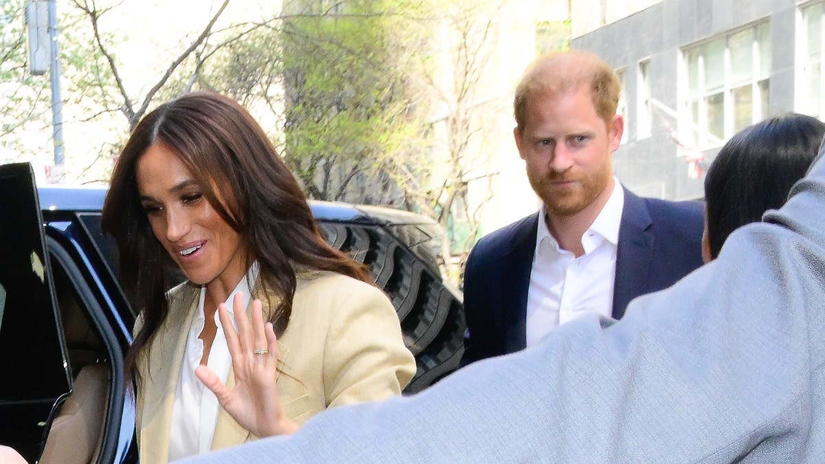 Meghan Markle waving entering inside a car while a stern Prince Harry looks on.