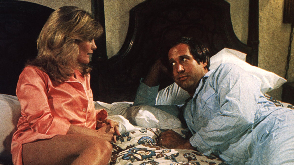 Beverly D'Angelo wearing an orange robe in bed with Chevy Chase.