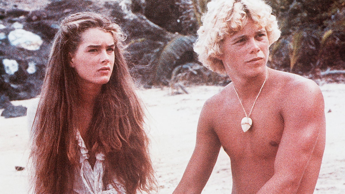 Christopher Atkins and Brooke Shields on the beach looking surprised.