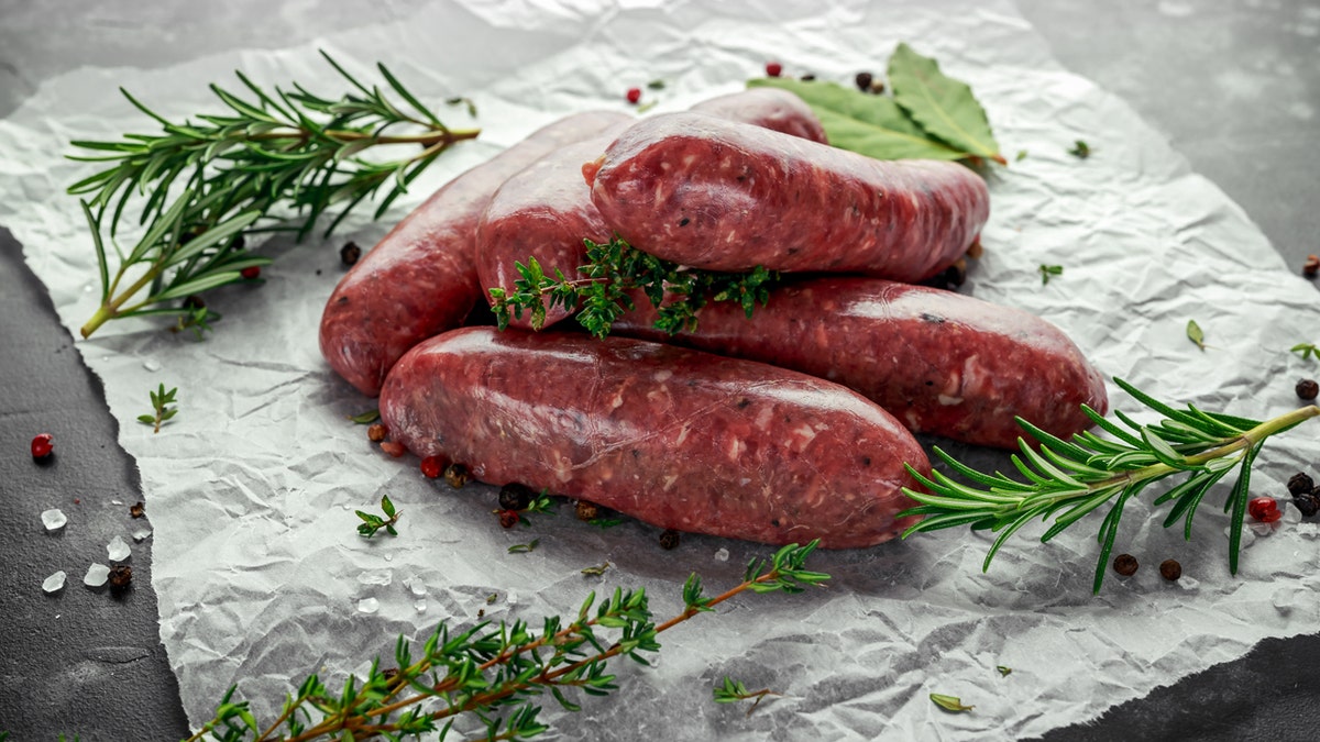 Freshly made raw butcher's sausages in skins with herbs on crumpled paper.