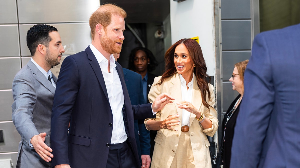 Meghan Markle walking outside with Prince Harry in New York City surrounded by bodyguards.
