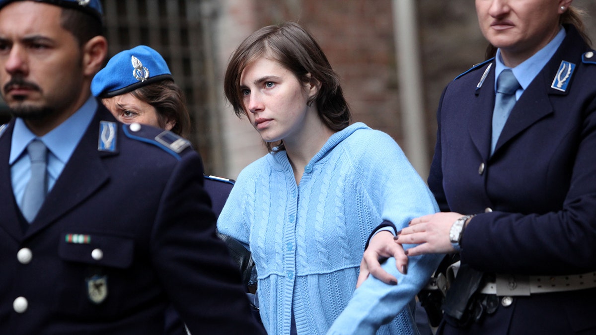 Amanda Knox in a light blue sweater being escorted by priests.