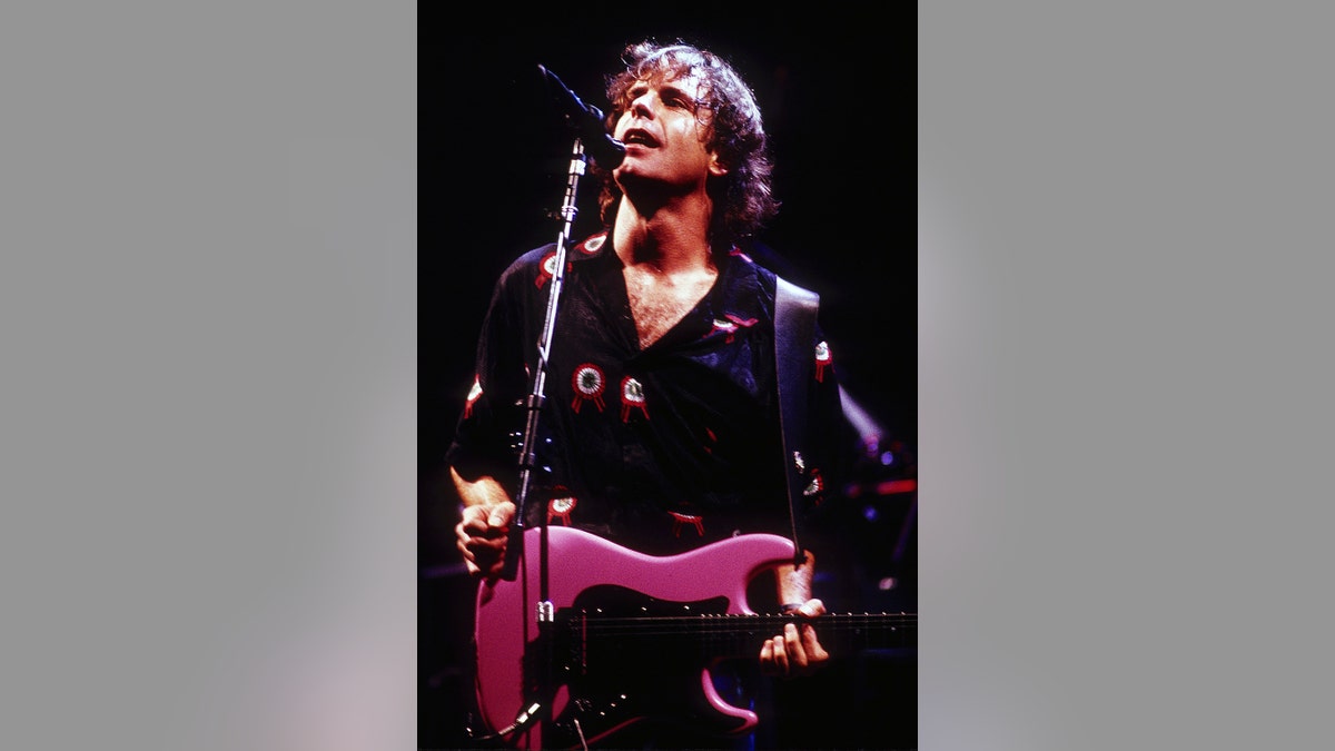 Bob Weir performing on stage and holding a pink guitar.